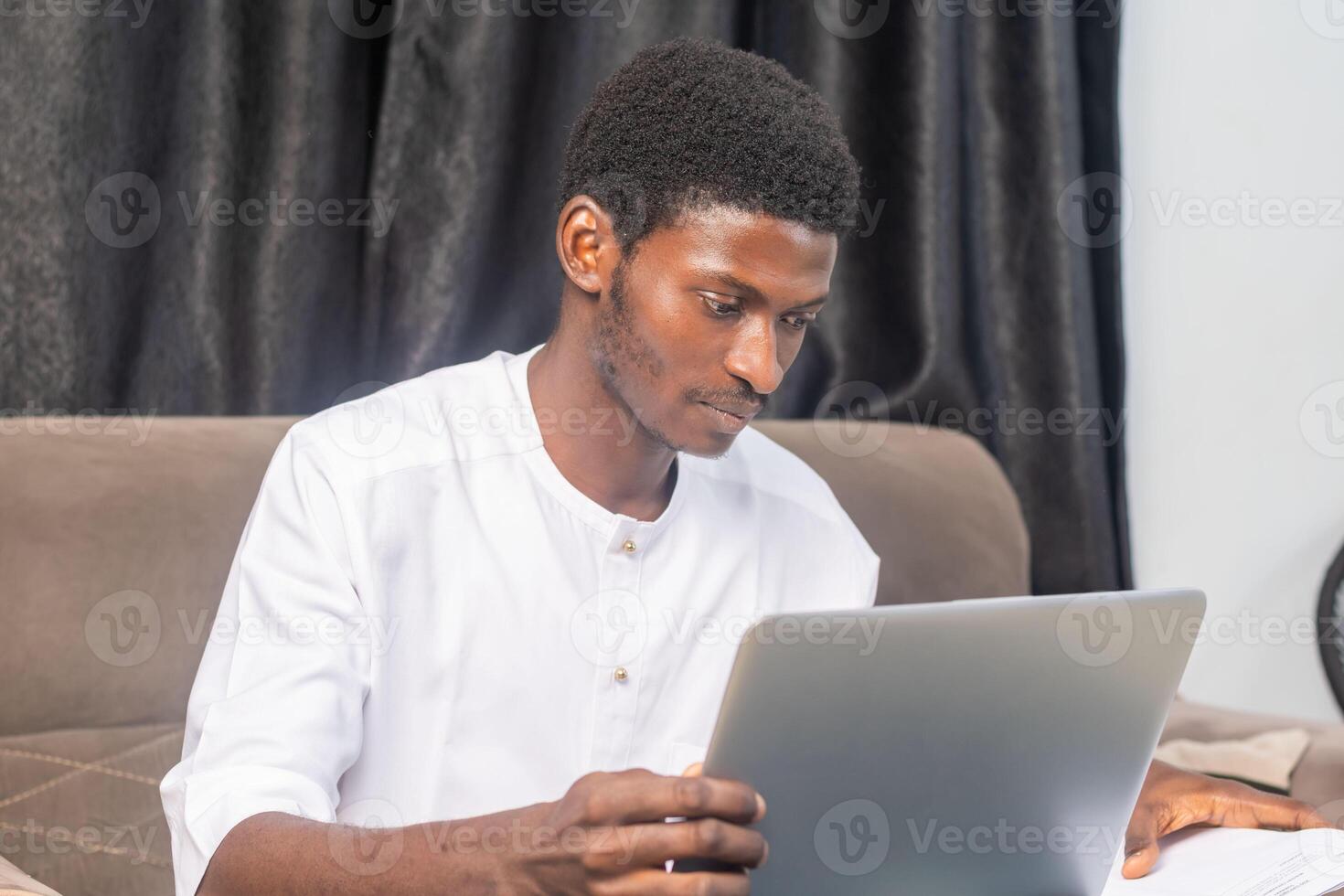 Young man smiling as he reads the screen of a laptop computer while relaxing on a comfortable couch at home photo