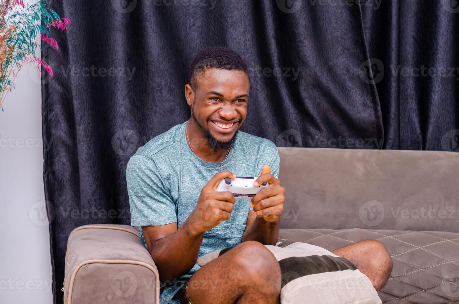 African American young joyful man resting at home sitting on couch and playing games photo