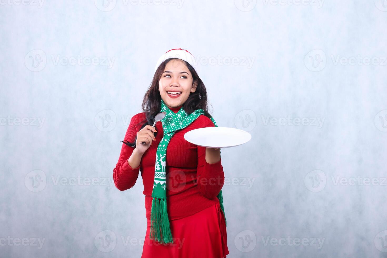portrait of woman wearing red sweater red sweater with santa hat and scarf celebrating merry christmas and new year, cheerful get idea carry white plate and hold spoon, isolated on white background photo