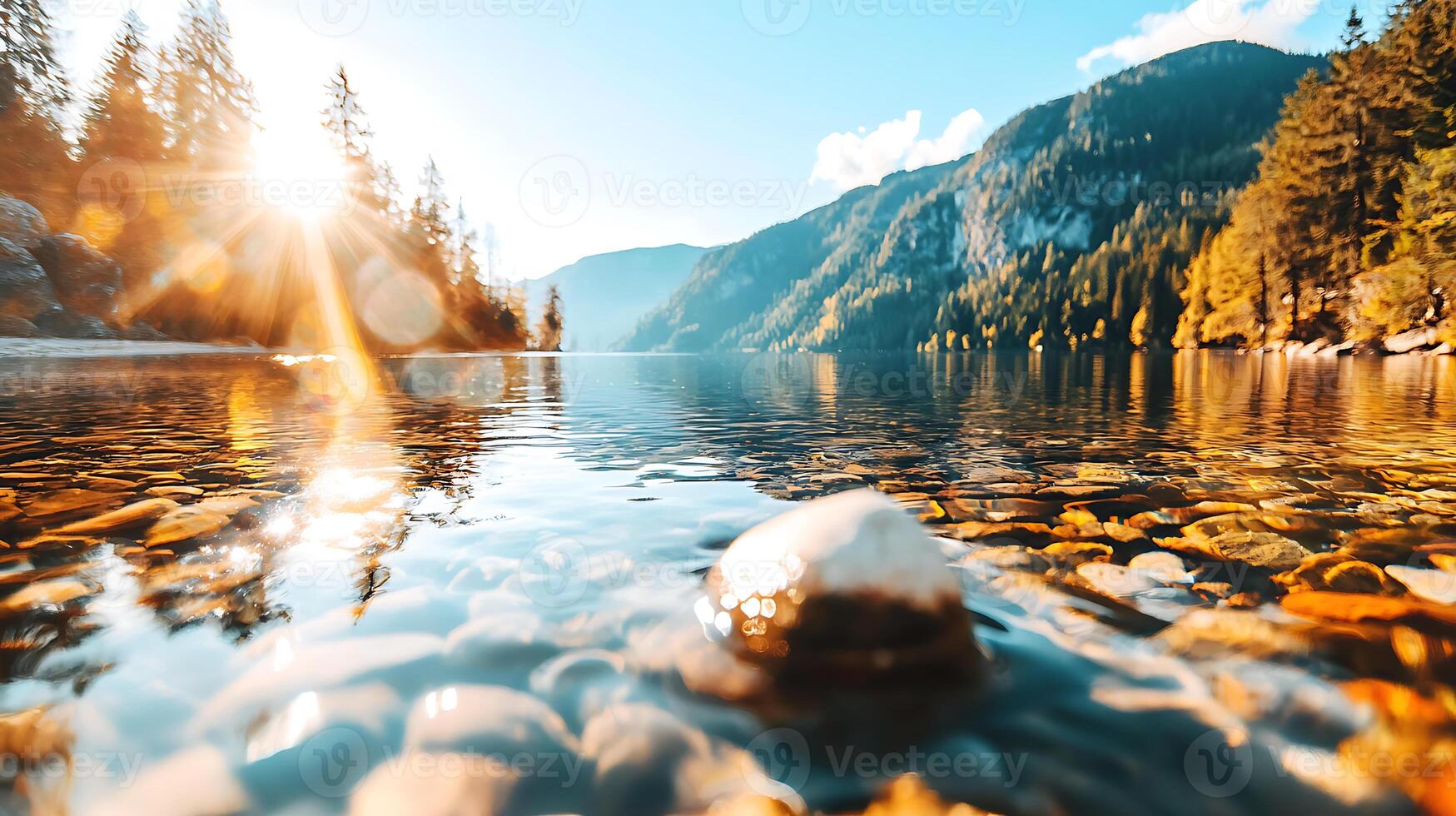 serene mountain lake reflects sky, surrounded by trees and sunlight. clear water reveals smooth stones beneath, creating tranquil atmosphere photo