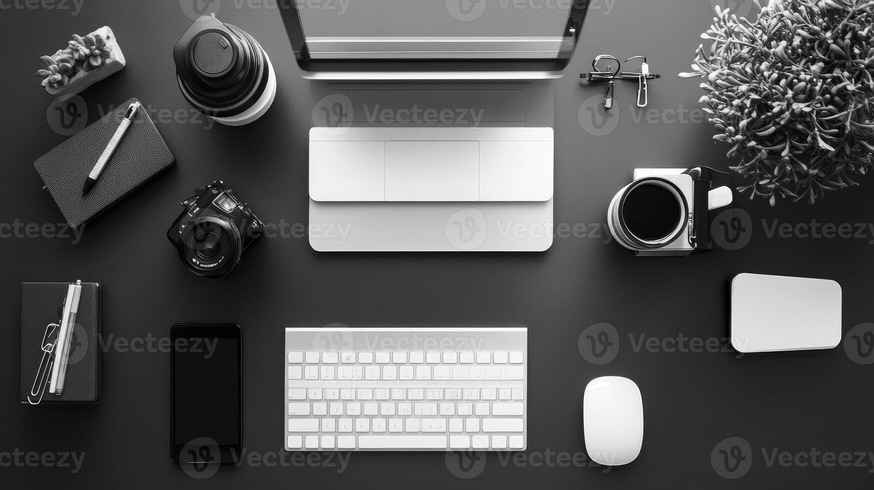 A black and white photo of a desk with a laptop, camera, and other items