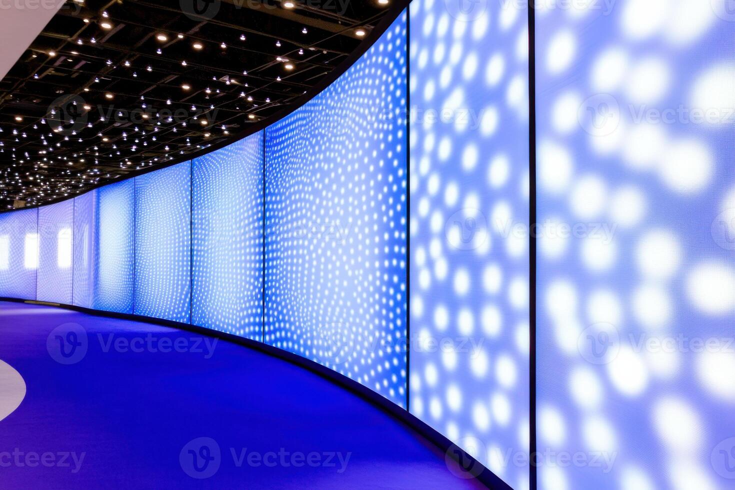 Bright blue LED screens illuminate a vibrant tech exhibition booth with dark blue backdrops and red branding in a modern setting photo