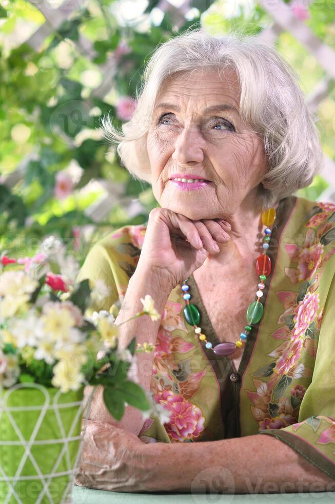 Beautiful elderly woman sits at a table in the summer at the country house photo