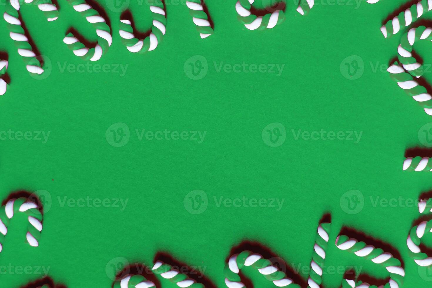 Flat lay Christmas composition with frame of candy canes on a green background. photo