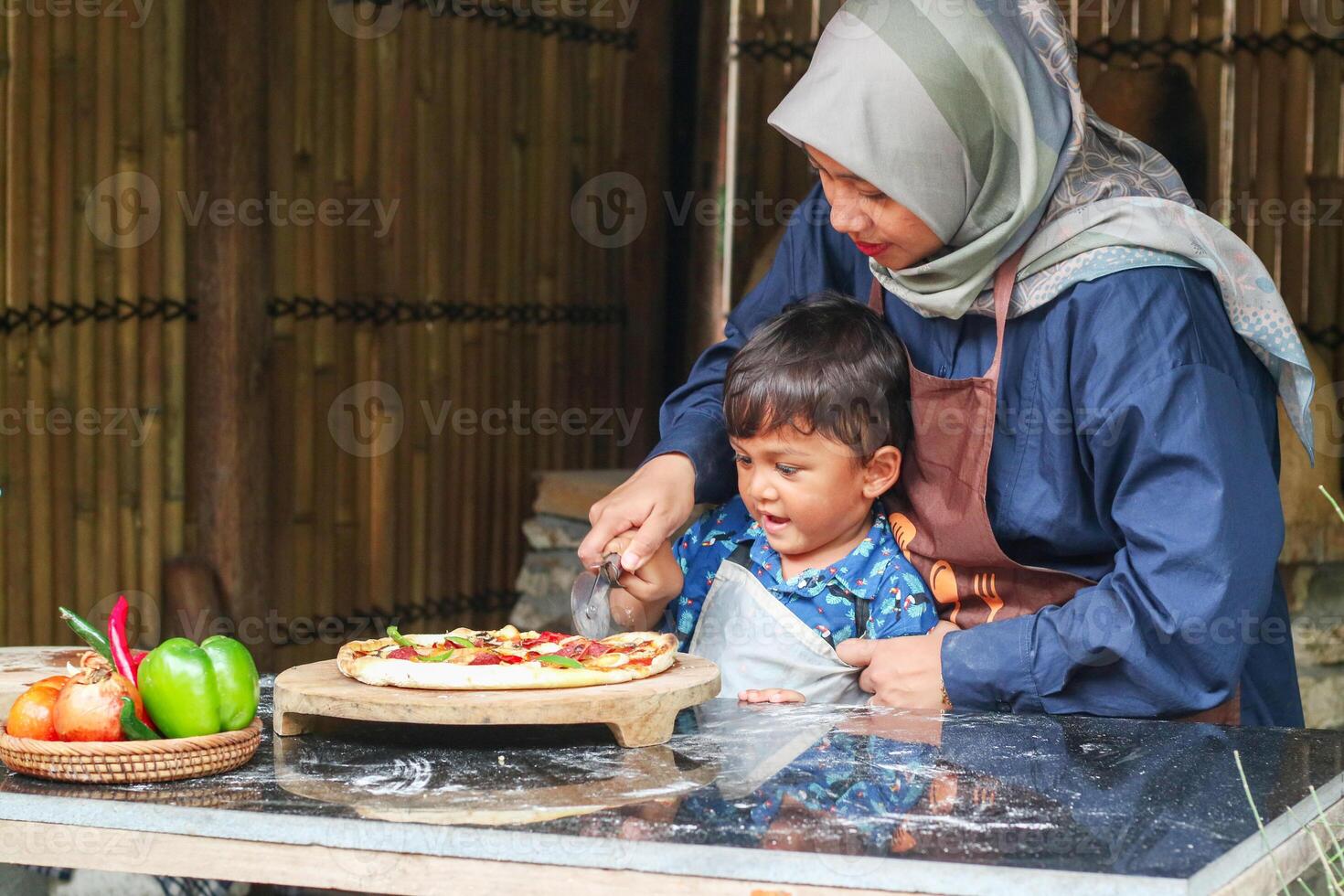 Asian Muslim Mother And Little son Rolling Up Dough On Table While Baking In Kitchen Together, Cute Small Girl And Islamic Mom In Hijab Having Fun At Home, Enjoying Preparing Homemade Pastry photo