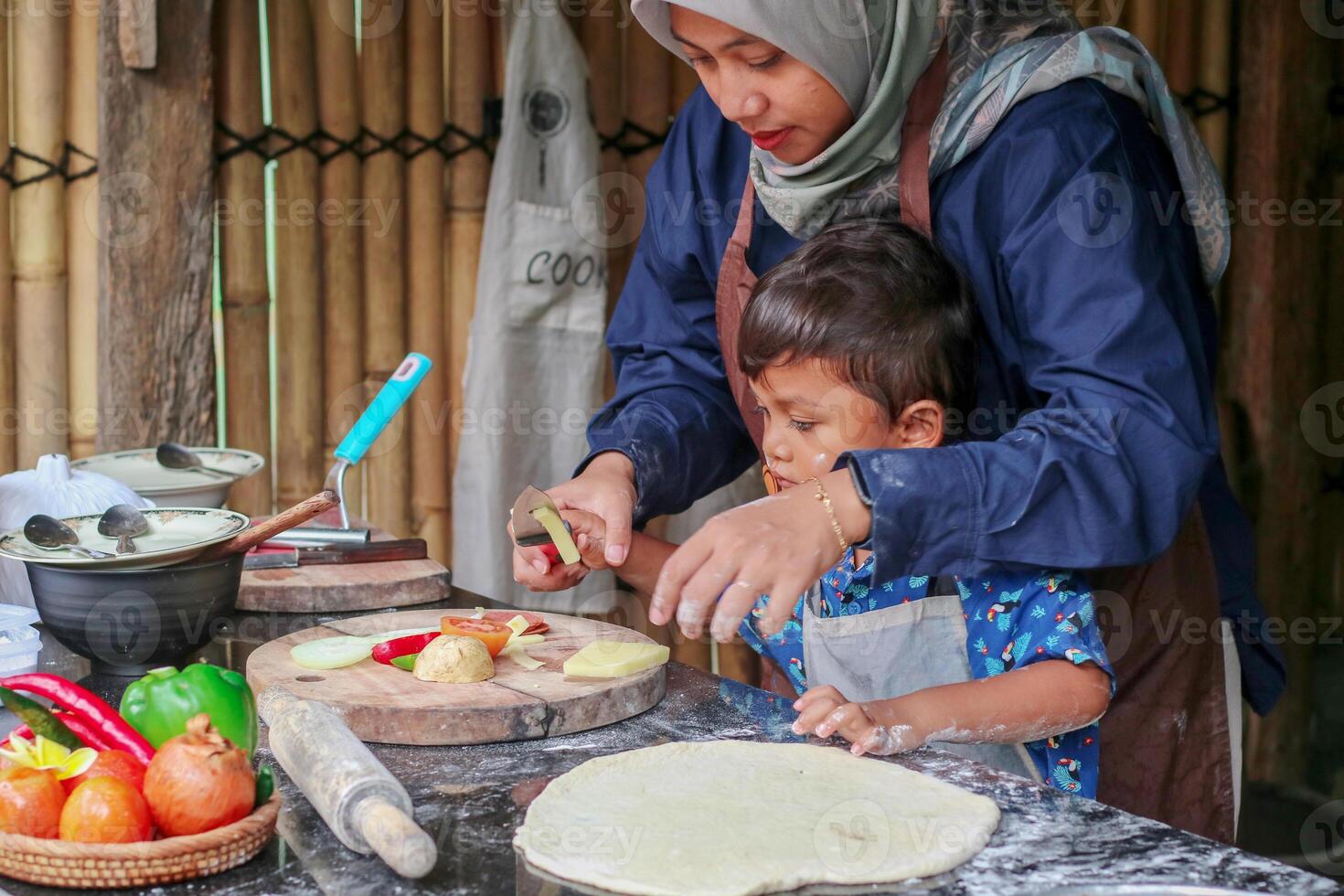 Happy family adult parent hijab mom teaching small child son doing bakery, cute little kid boy hold rolling pin roll dough having fun helping mum learning bake pastry make pie or biscuits in kitchen photo