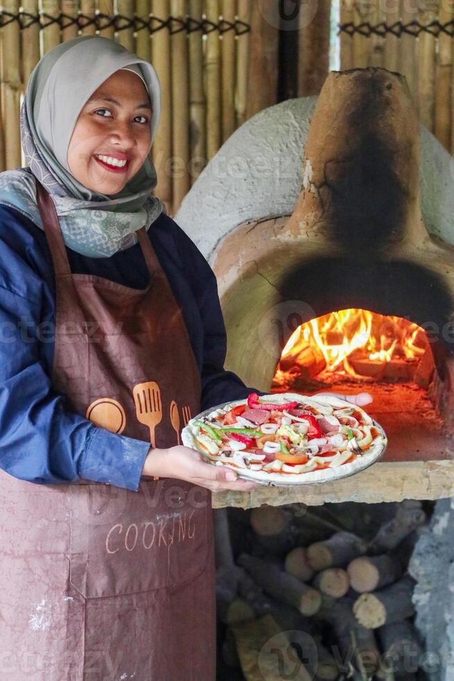 A process of preparing pizza by a asian hijab girl. Italian traditional pizza is cooked in a stone wood-fired oven. photo