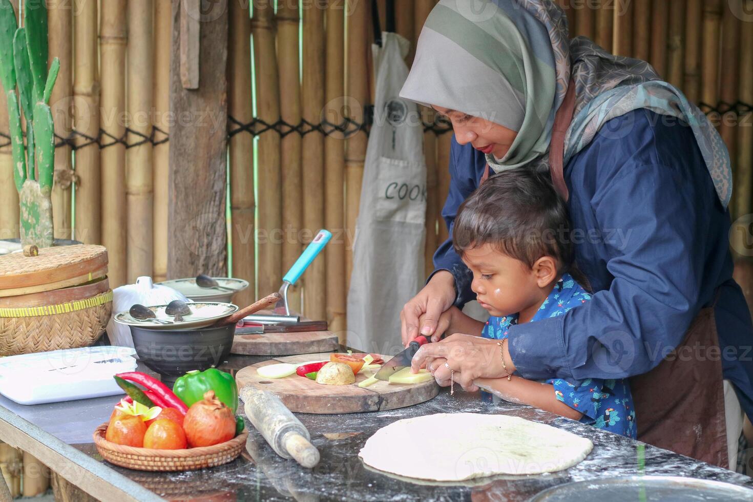 Happy family adult parent hijab mom teaching small child son doing bakery, cute little kid boy hold rolling pin roll dough having fun helping mum learning bake pastry make pie or biscuits in kitchen photo