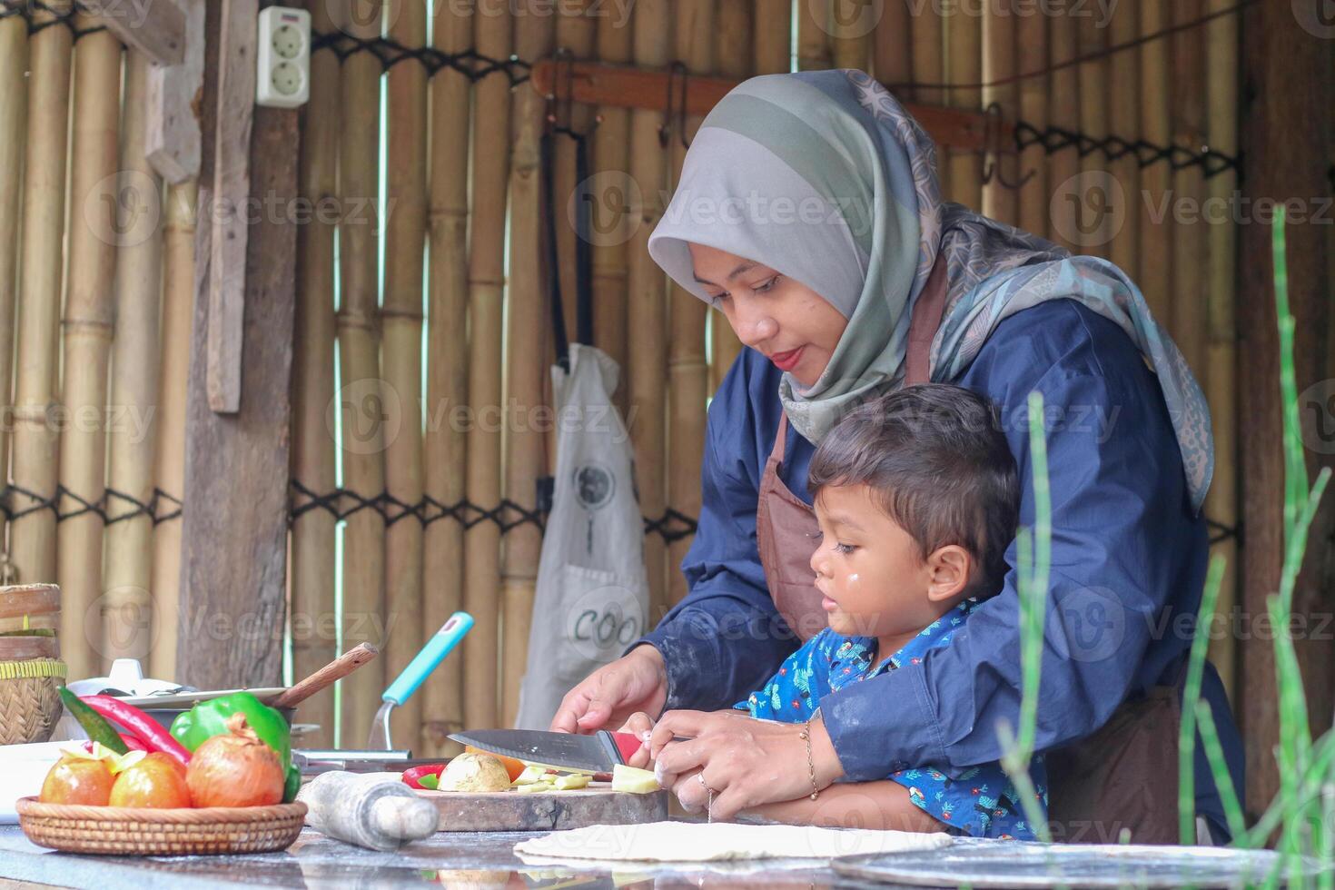 Happy family adult parent hijab mom teaching small child son doing bakery, cute little kid boy hold rolling pin roll dough having fun helping mum learning bake pastry make pie or biscuits in kitchen photo