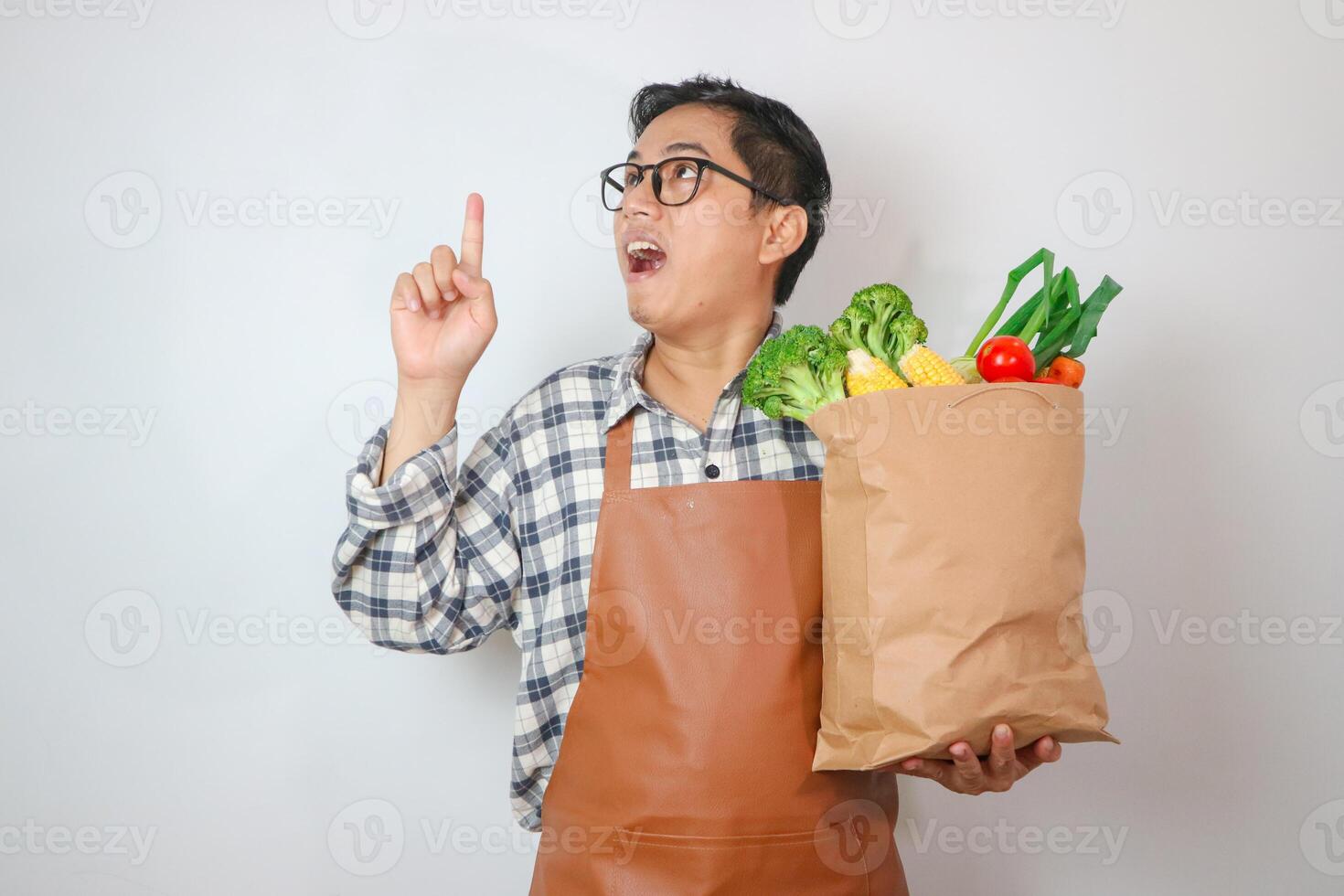 Asian Man apron thinking gesture to grocery shopping bag with finger up with great new idea isolated on plain pastel white photo
