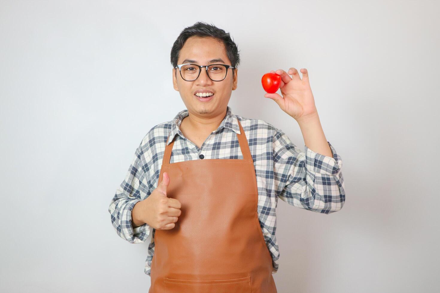 asian man with apron holding red tomato give hand thumb up photo