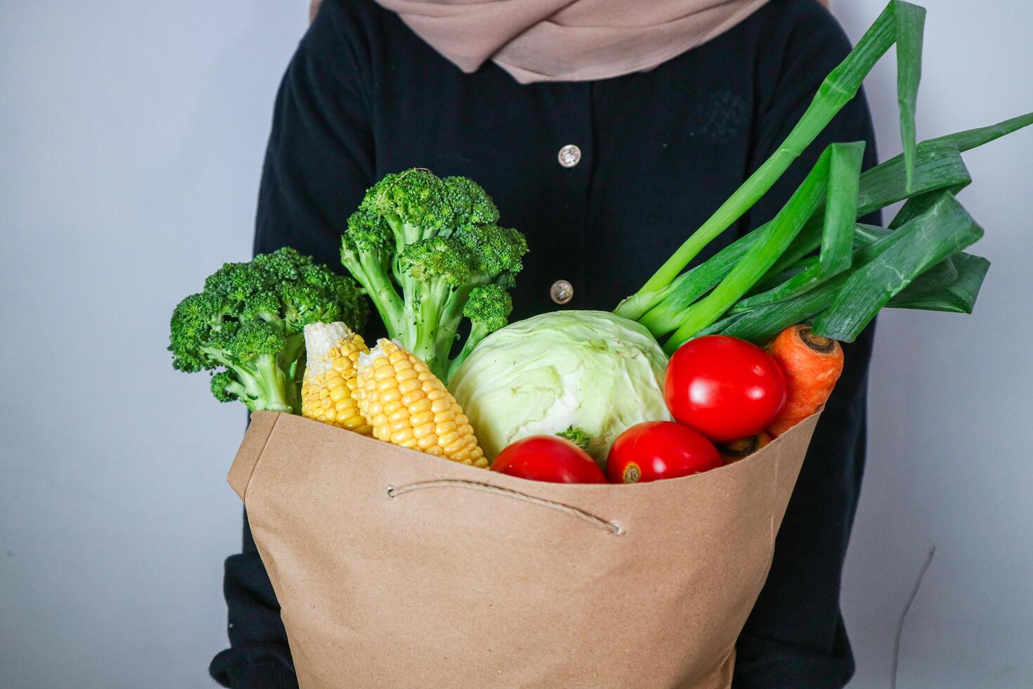 Asian girl Holding Paper Bag With Groceries In Kitchen Interior, Closeup Shot Of Mature Male Carrying Pack With Fresh Organic Vegetables And Fruits On Table photo