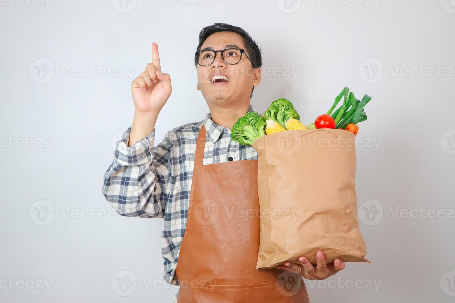 Asian Man with apron thinking gesture to grocery shopping bag with finger up with great new idea isolated on plain white photo