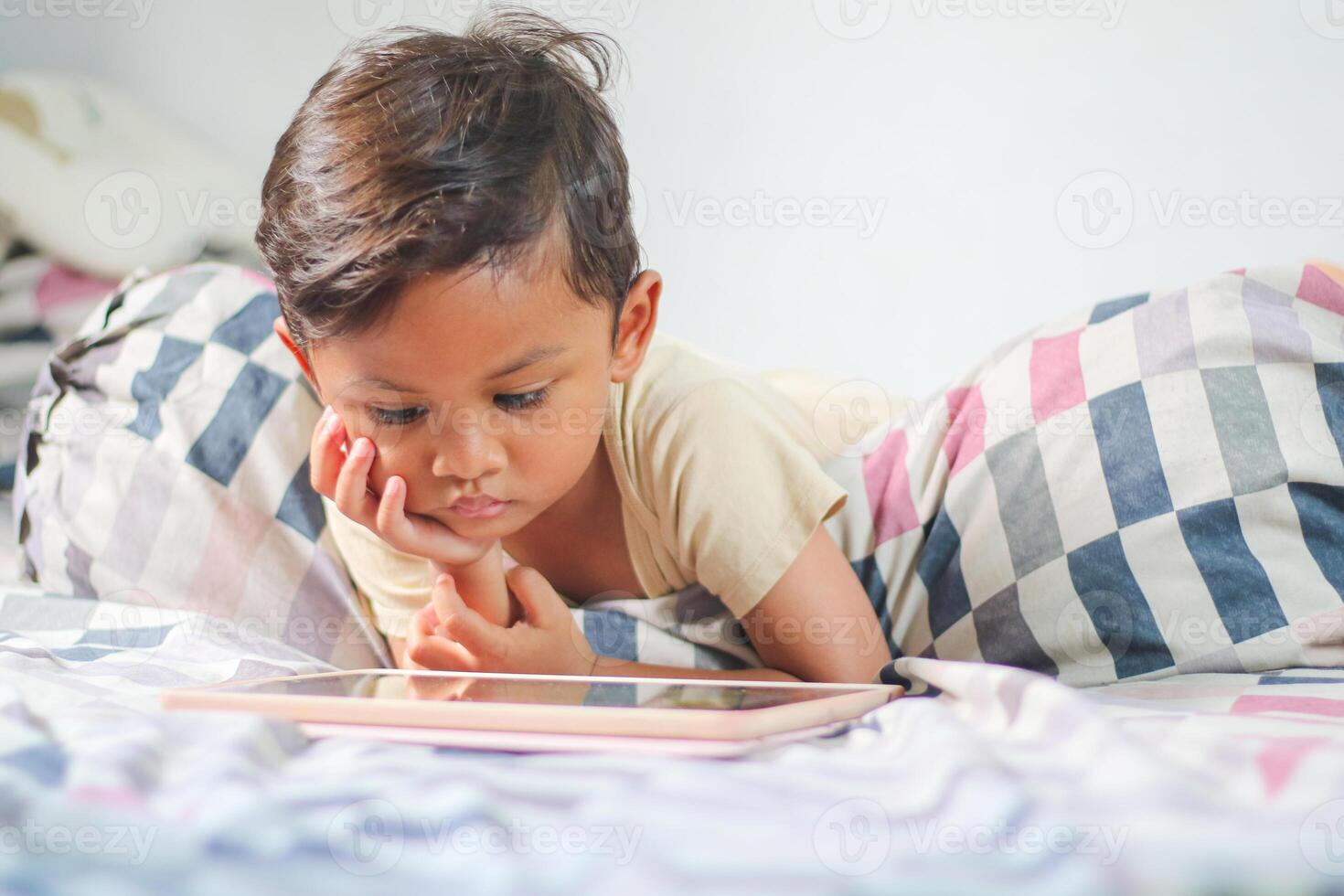 three year old Asian boy at home bed using digital tablet computer photo