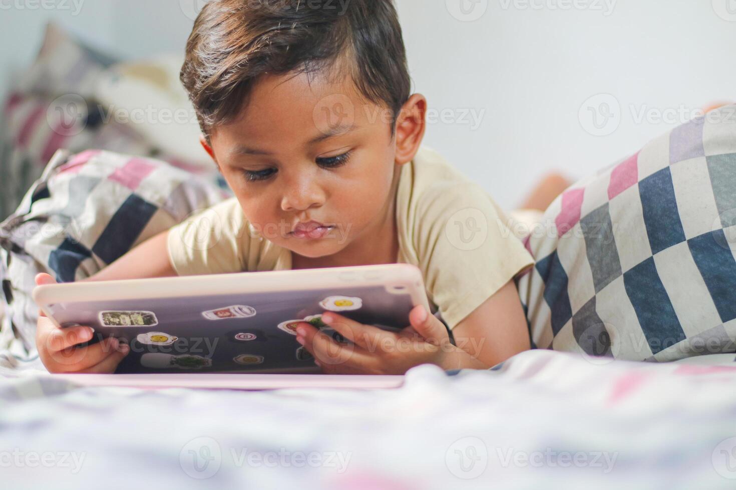 three year old Asian boy at home bed using digital tablet computer photo