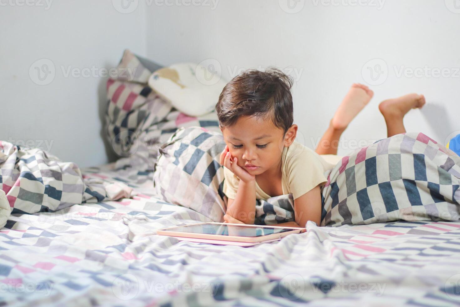 three year old Asian boy at home bed using digital tablet computer photo