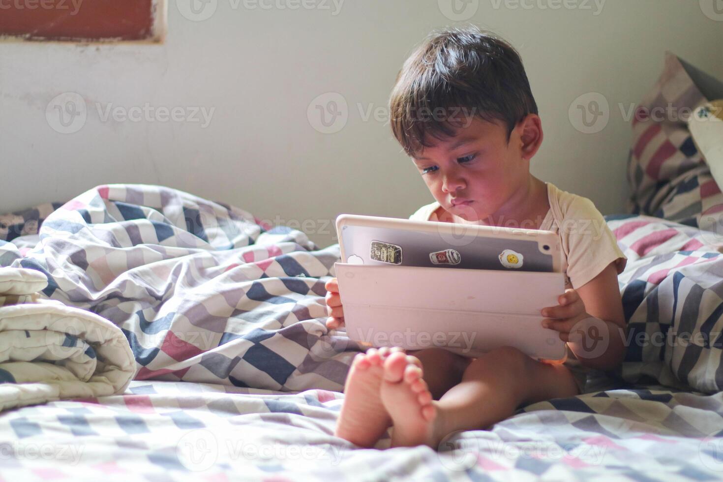 three year old Asian boy at home bed using digital tablet computer photo