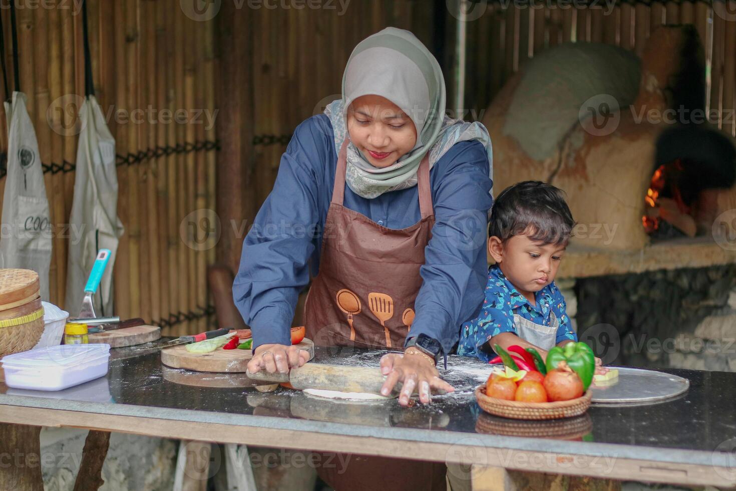 Cute asian little boy and muslim mom in hijab rolling up dough on table in kitchen together, enjoying preparing homemade pastry, happy islamic mother and child cooking and having fun at home photo