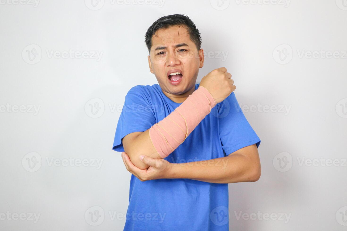 A resilient male with broken arm maintains smile while wearing splint for treatment, coping with discomfort. An upbeat Asian man in an arm sling on white background, symbolizing injury recovery. photo