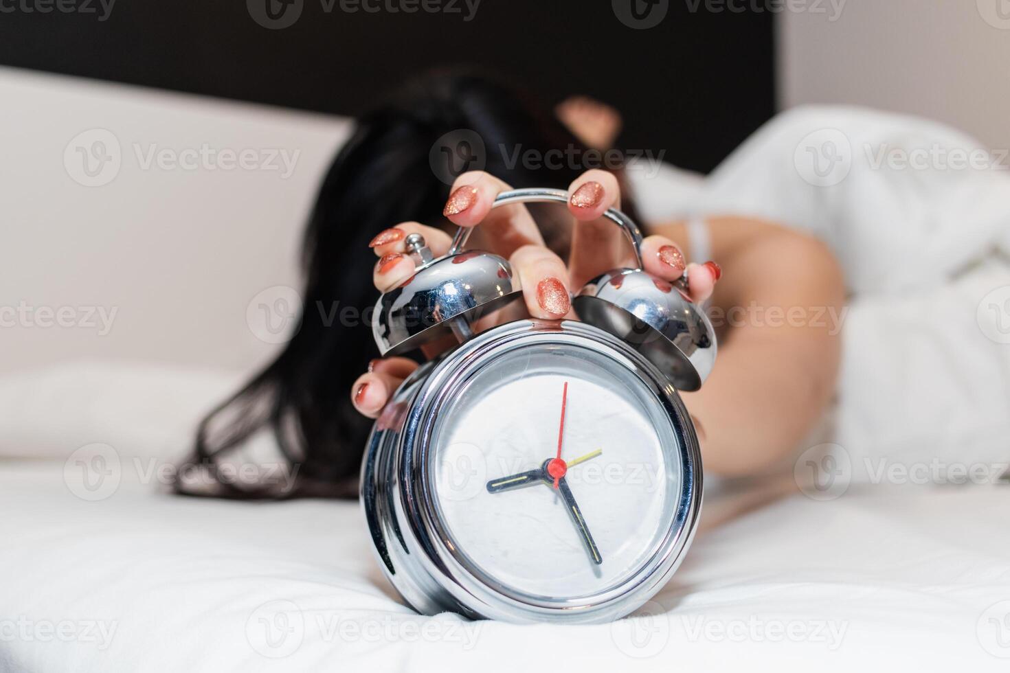 The girl's hand held the alarm clock on the mattress in the bedroom. A young girl had to wake up in the morning to turn off the alarm clock that had been set to wake up in the morning. photo