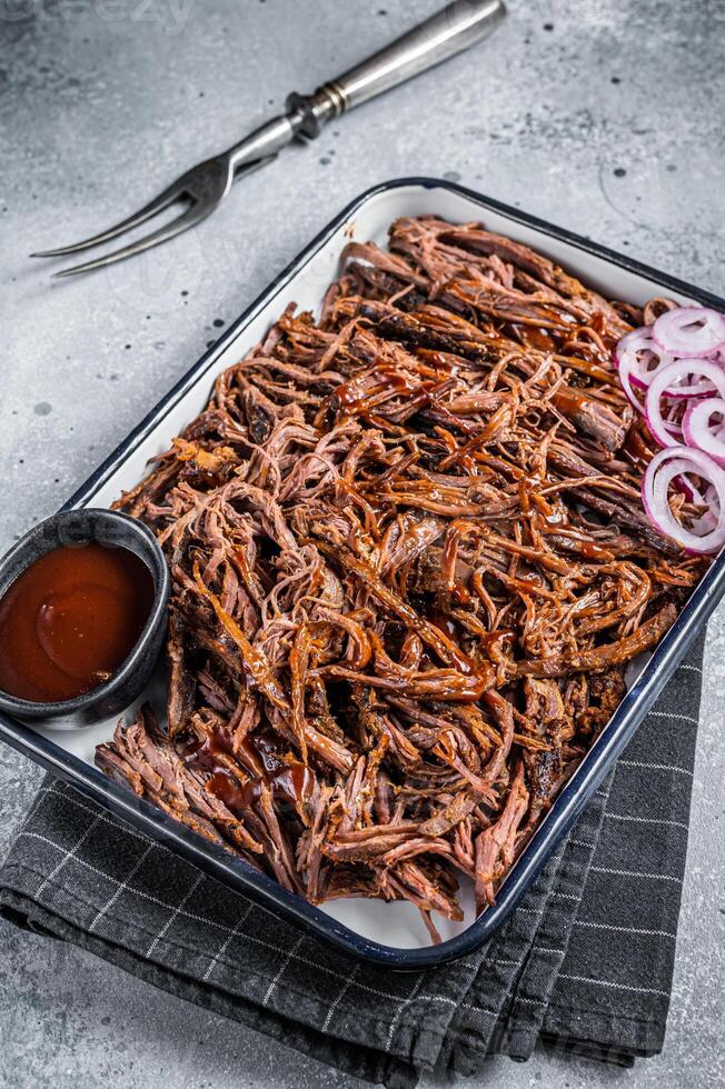 Pulled beef meat with hot chili sauce in baking dish. Gray background. Top view photo