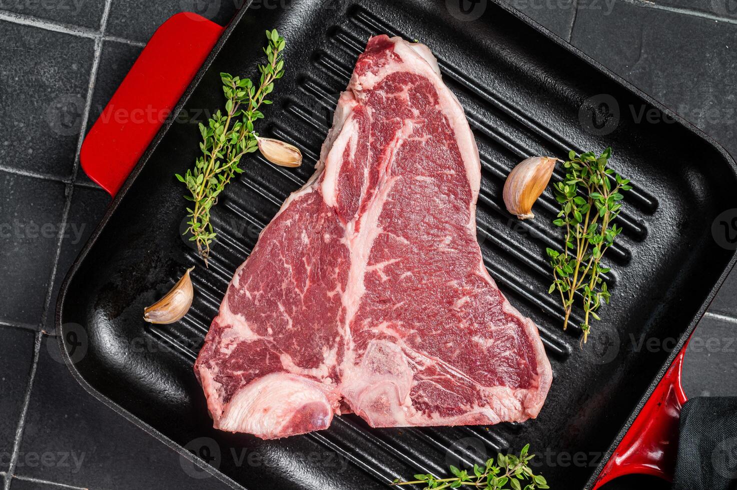 Raw T-bone or porterhouse beef meat Steak with thyme in a grill skillet ready for cooking. Black background. Top view photo