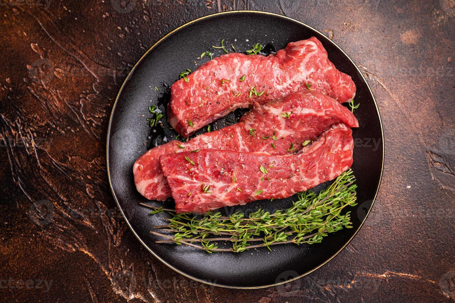 Tri tip steaks, Raw marbled beef meat on plate with herbs. brown background. top view photo