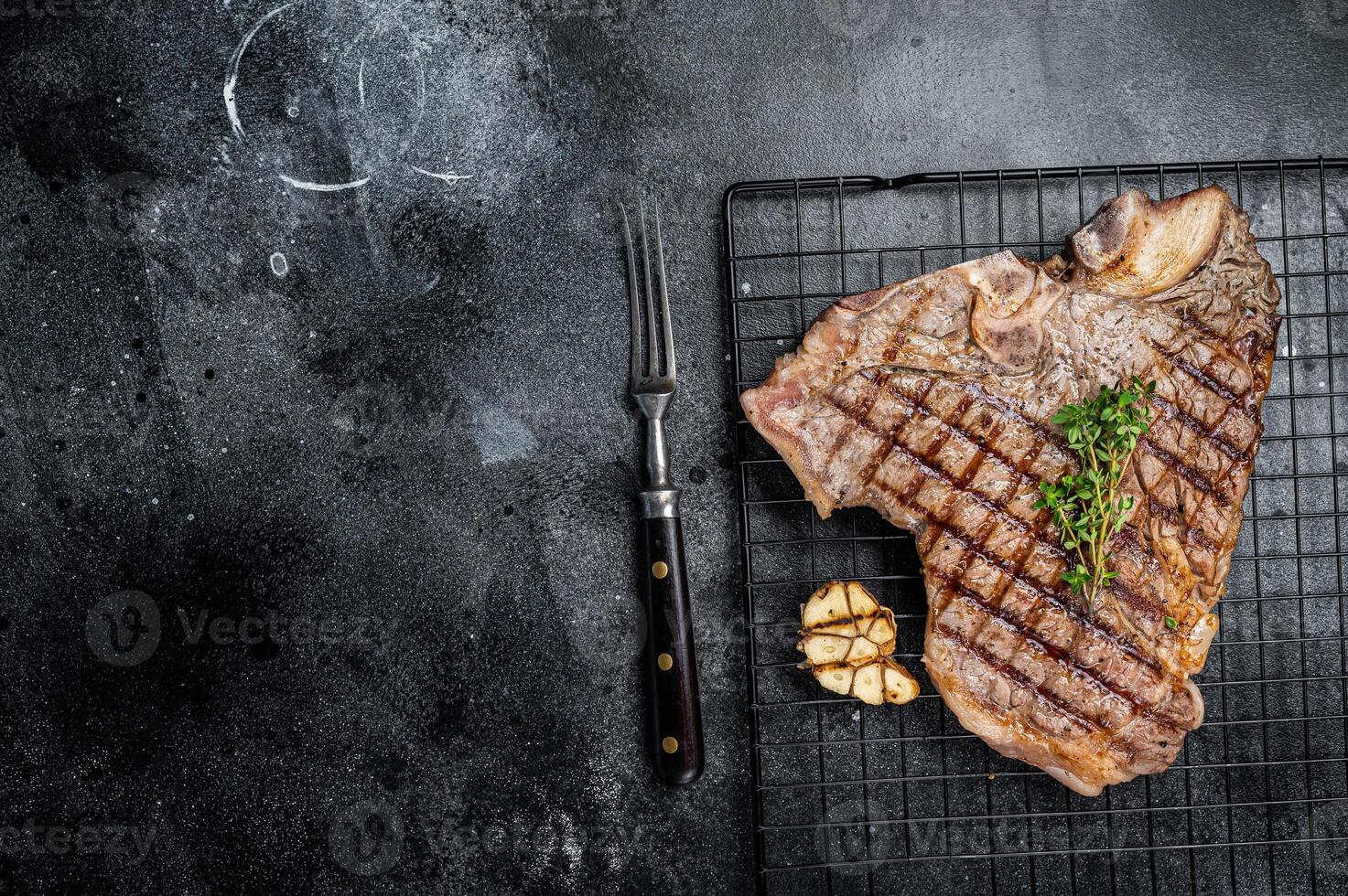 Grilled T-bone or Porterhouse beef meat Steak on a rack. Black background. Top view. Copy space photo