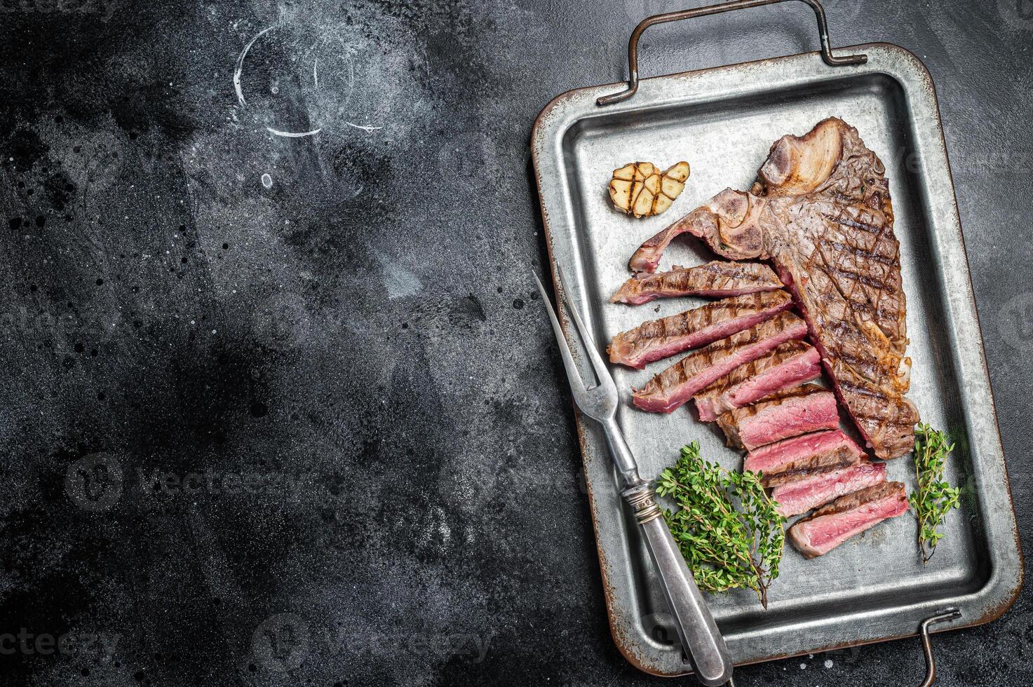 Medium rare Grilled T-Bone Steak, Florentine steak sliced in a steel tray. Black background. Top view. Copy space photo