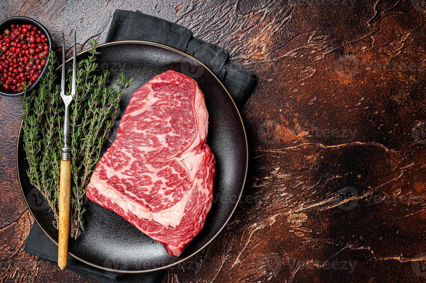 Black Angus Rib Eye steak, raw marbled beef meat with herbs. Dark background. Top view. Copy space photo