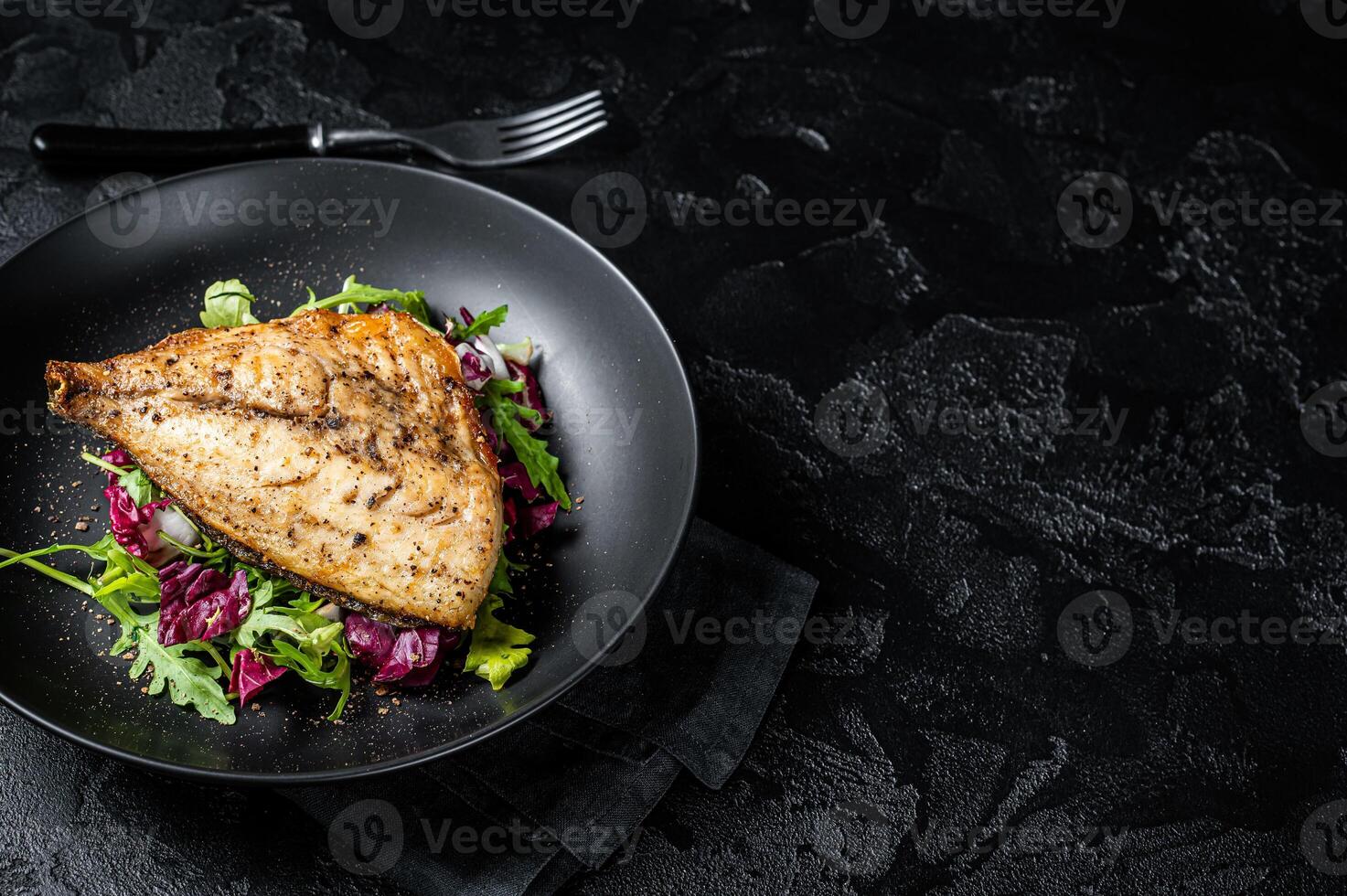 Grilled Sea Bream Dorado fillets served on fresh salad. Black background. Top view. Copy space photo
