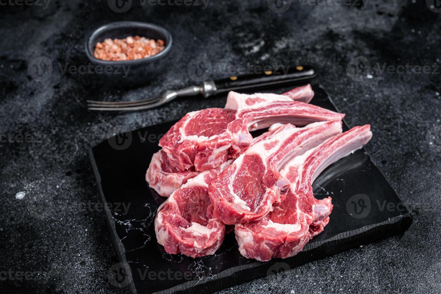 Uncooked lamb mutton chops, raw meat steaks. Black background. Top view photo