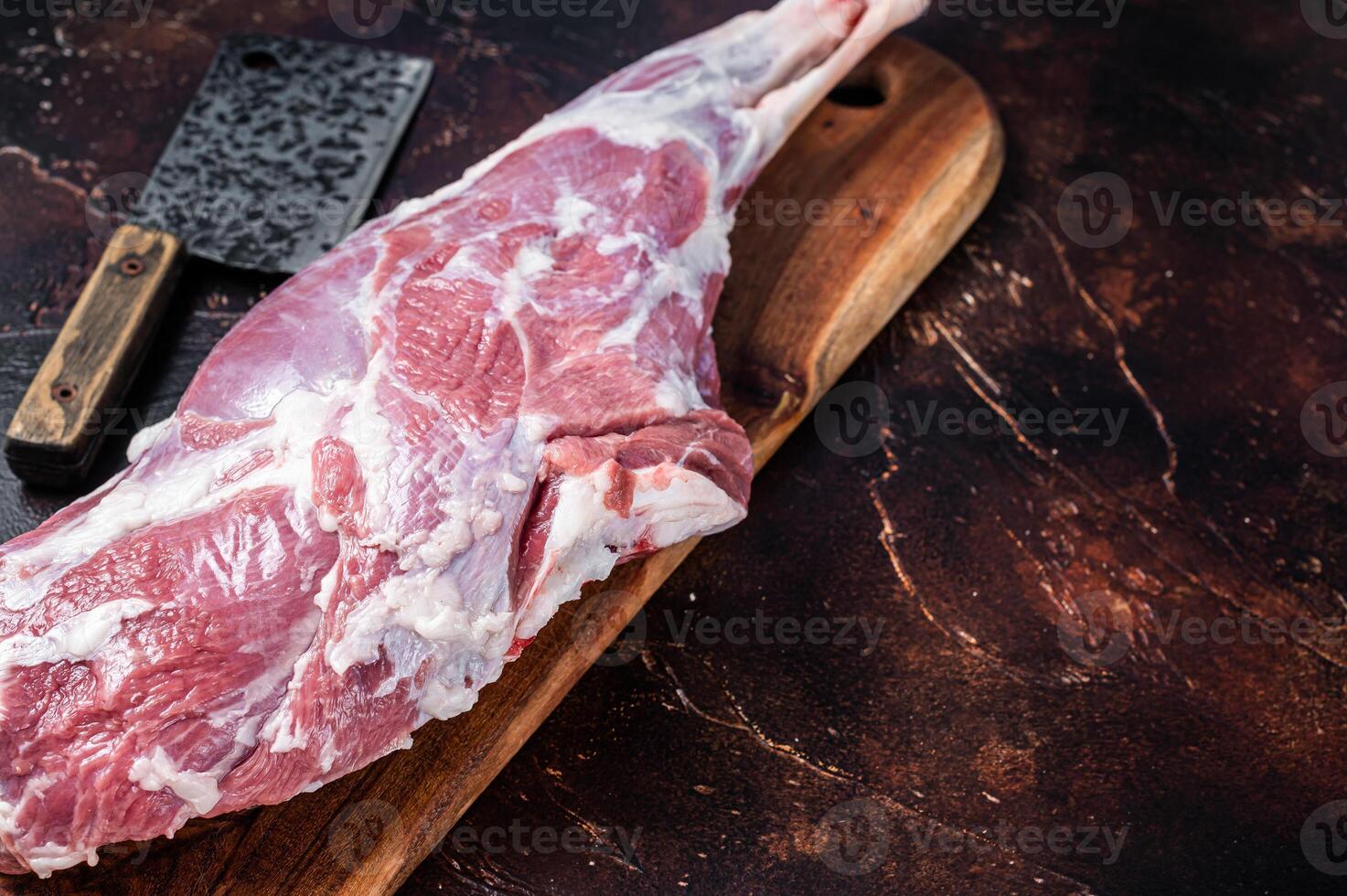 Raw whole lamb leg thigh on butcher board. Dark background. Top view. Copy space photo