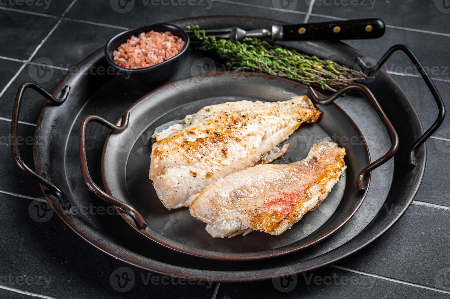 Roasted ocean red perch fillet with olive oil, thyme and spices. Black background. Top view photo