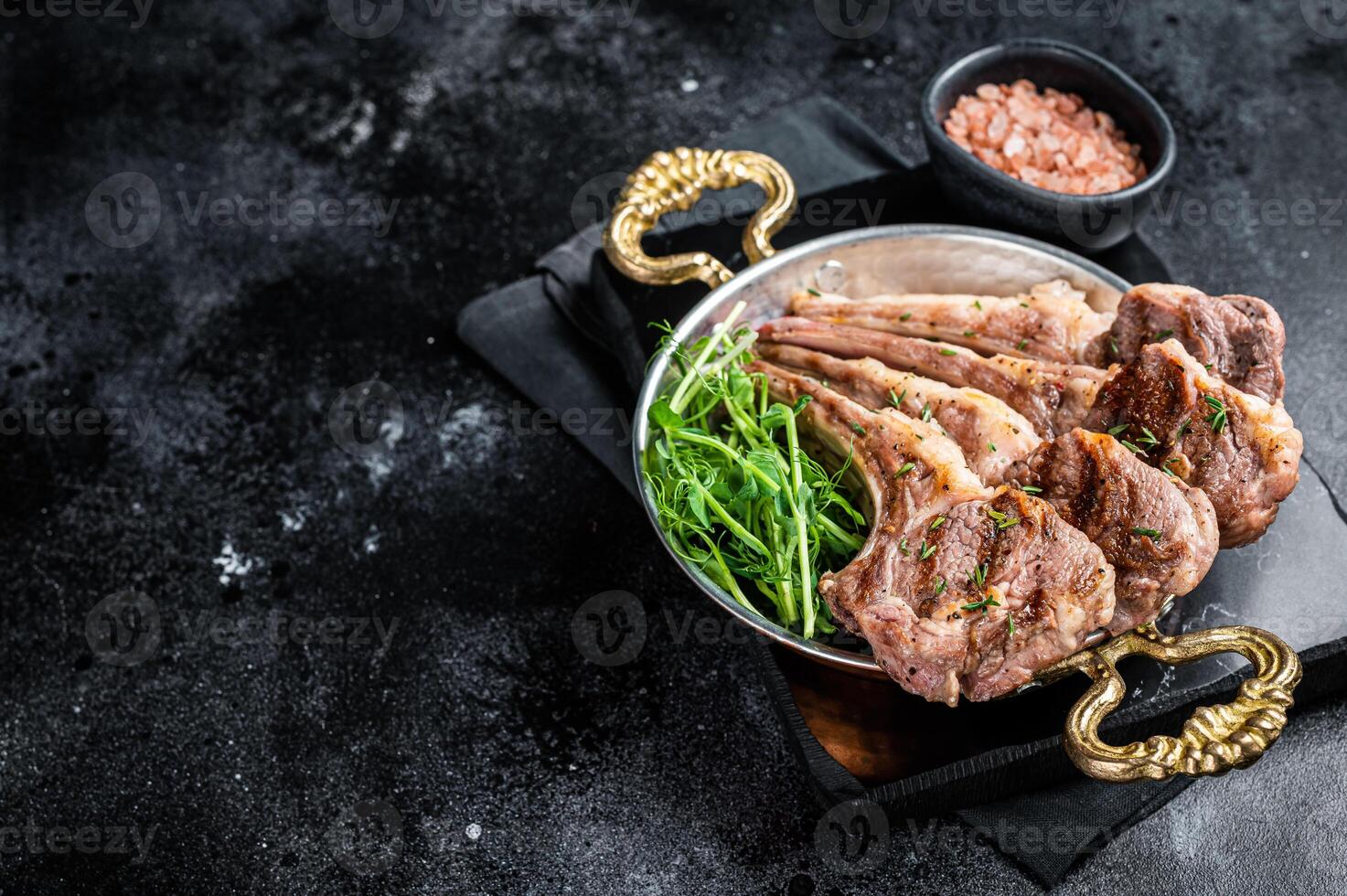 Grilled Lamb mutton Chops steaks in a skillet with green salad. Black background. Top view. Copy space photo