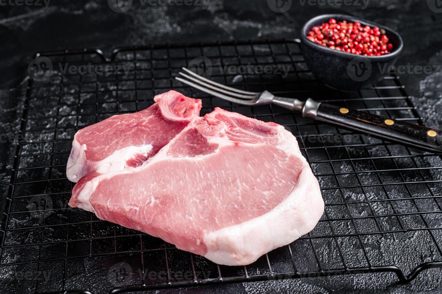 Uncooked Raw pork T bone chop meat steak on grill. Black background. Top view photo