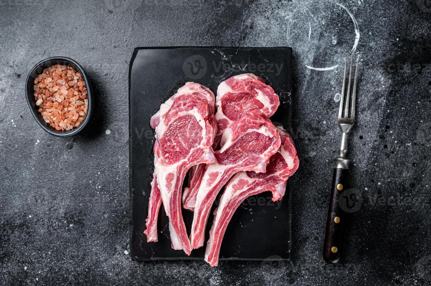 Uncooked lamb mutton chops, raw meat steaks. Black background. Top view photo