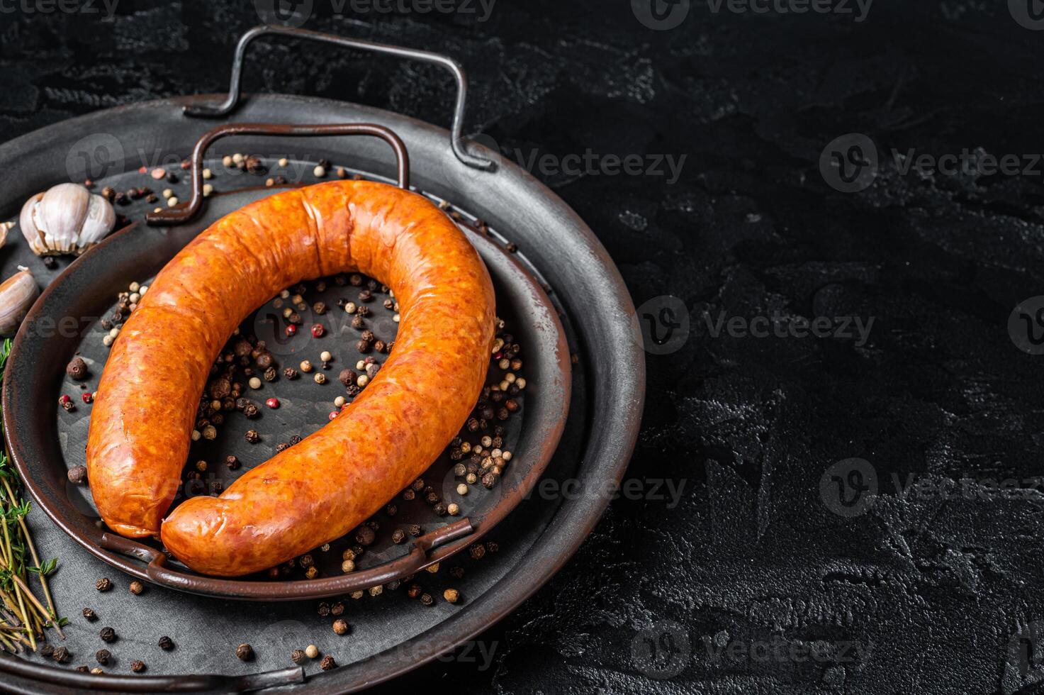Smoked sausage with thyme and spices in a steel tray. Black background. Top view. COpy space photo