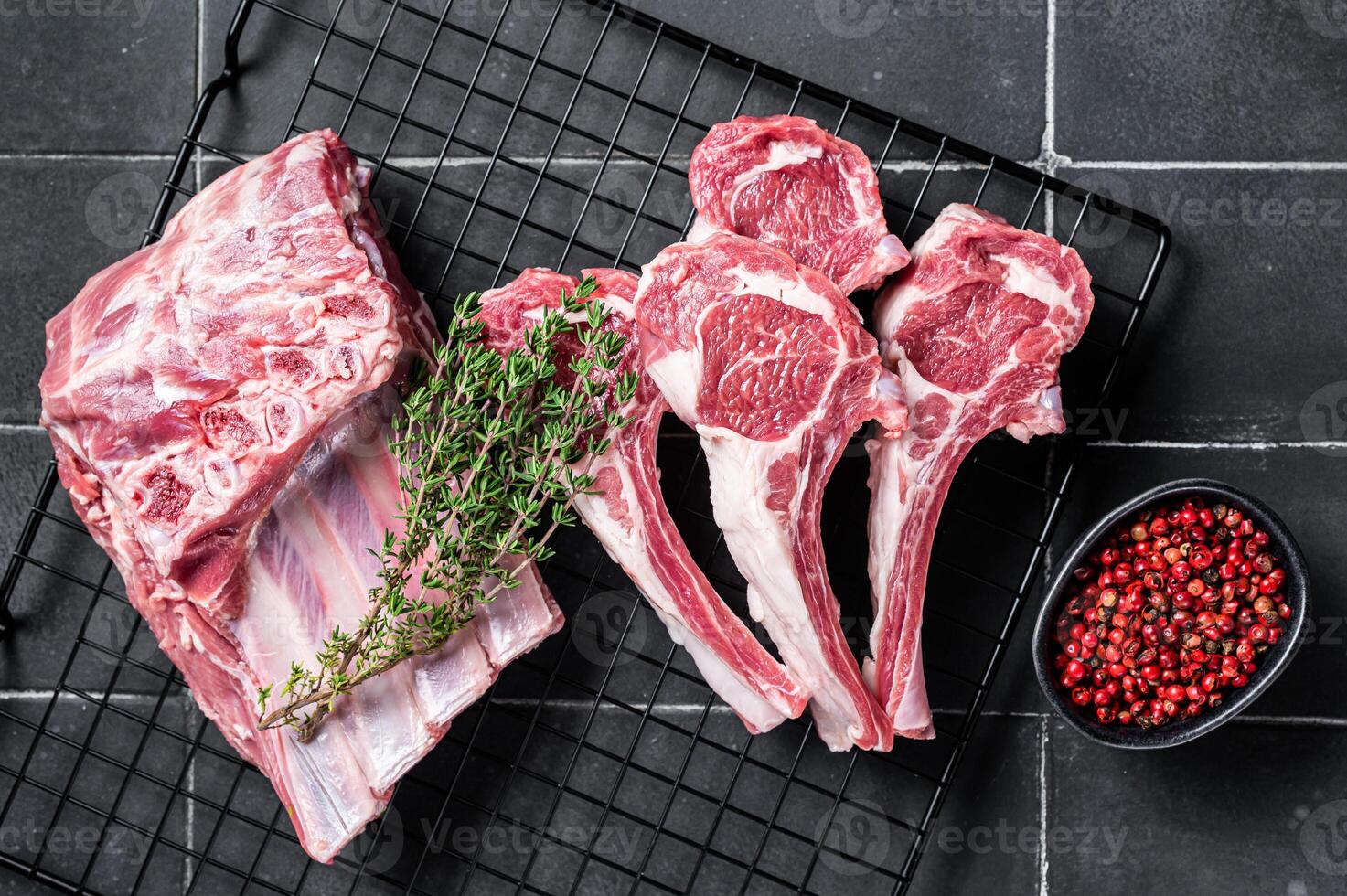 Fresh Raw lamb meat chop steaks on kitchen table with spices and herbs. Black background. Top view photo