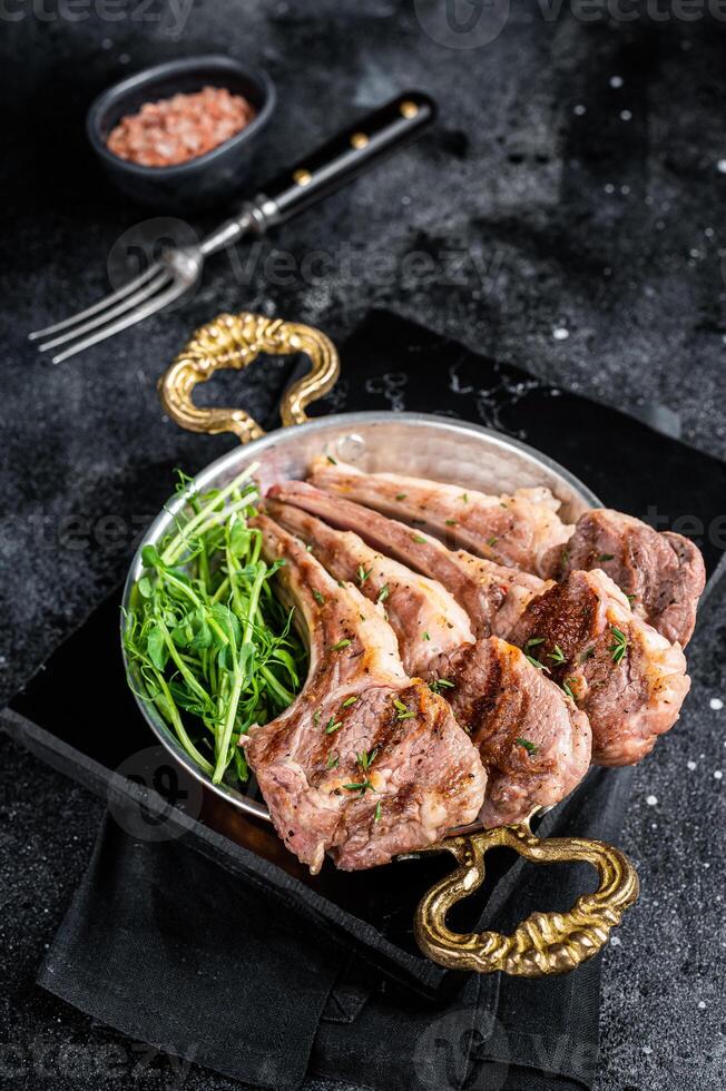 Grilled Lamb mutton Chops steaks in a skillet with green salad. Black background. Top view photo