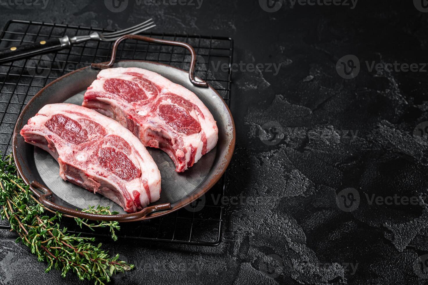 Raw fresh lamb loin chops with herbs and spices in steel tray. Black background. Top view. Copy space photo