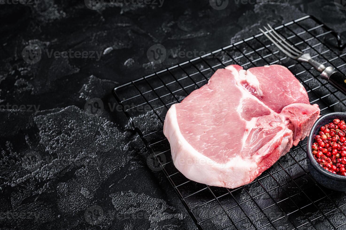 Uncooked Raw pork T bone chop meat steak on grill. Black background. Top view. Copy space photo
