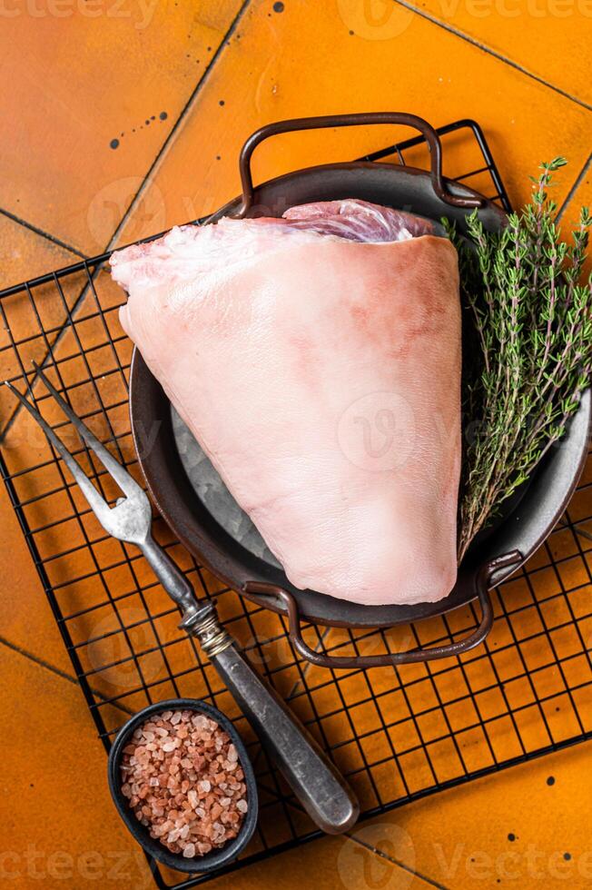 Raw pork shank knuckle in a steel tray with herbs. Orange background. Top view. photo