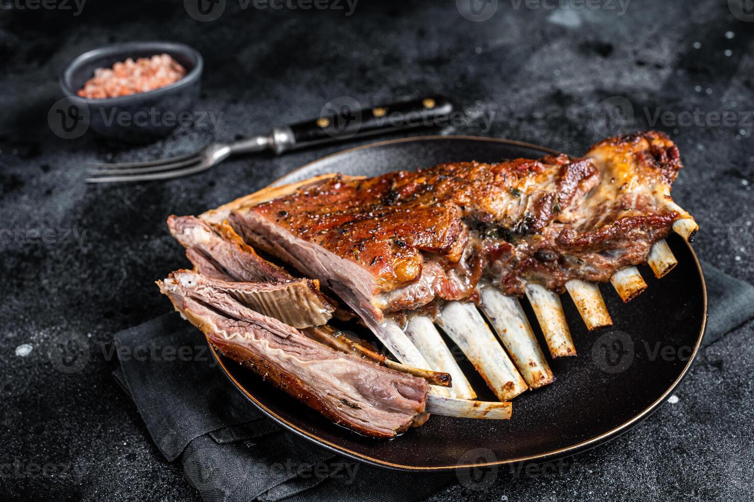 Roasted Rack of lamb ribs, mutton spareribs, sliced meat on plate. Black background. Top view photo