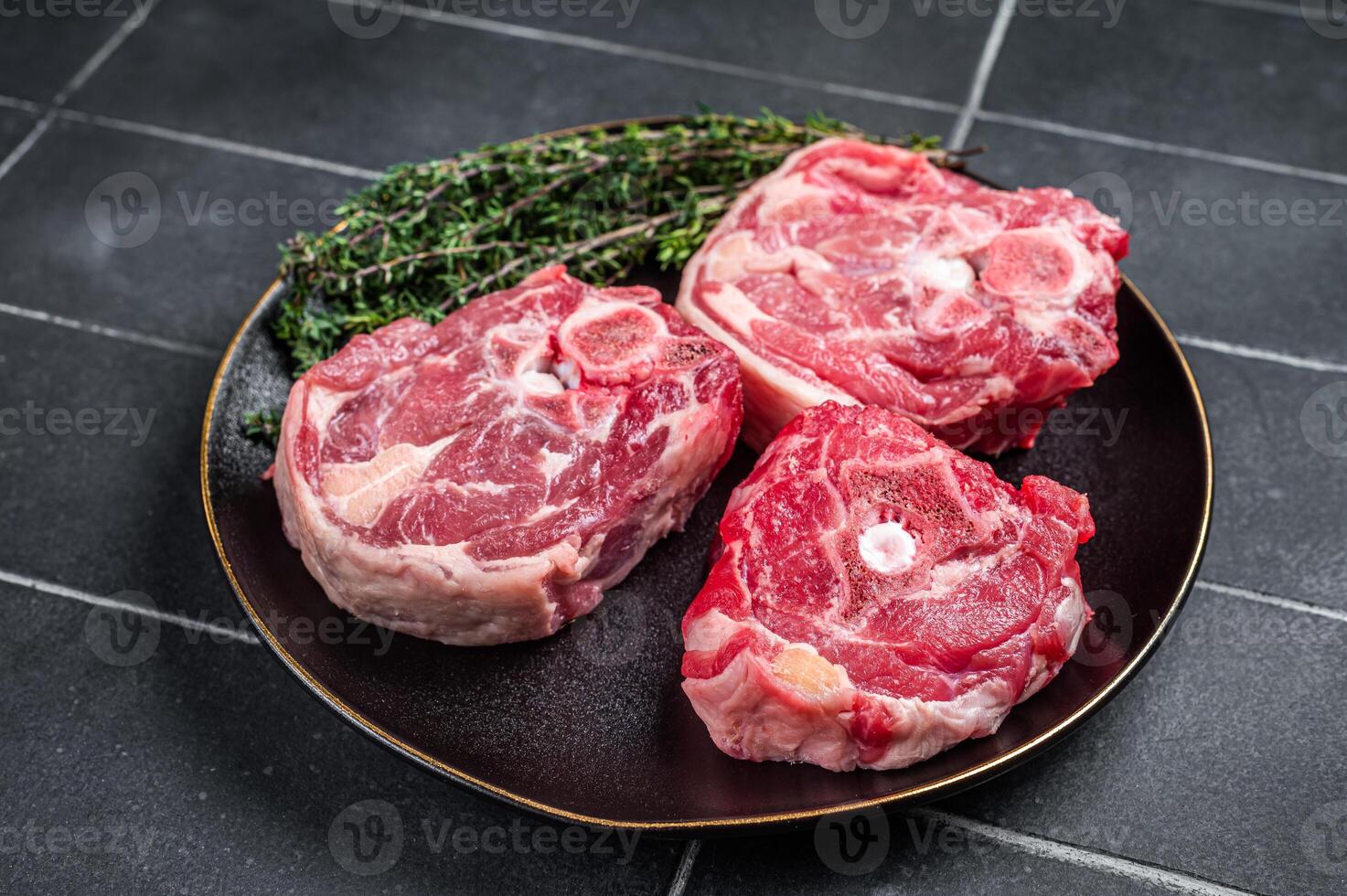 Raw Lamb Gerdan, lamb neck chops on a plate with herbs. Black background. Top view photo