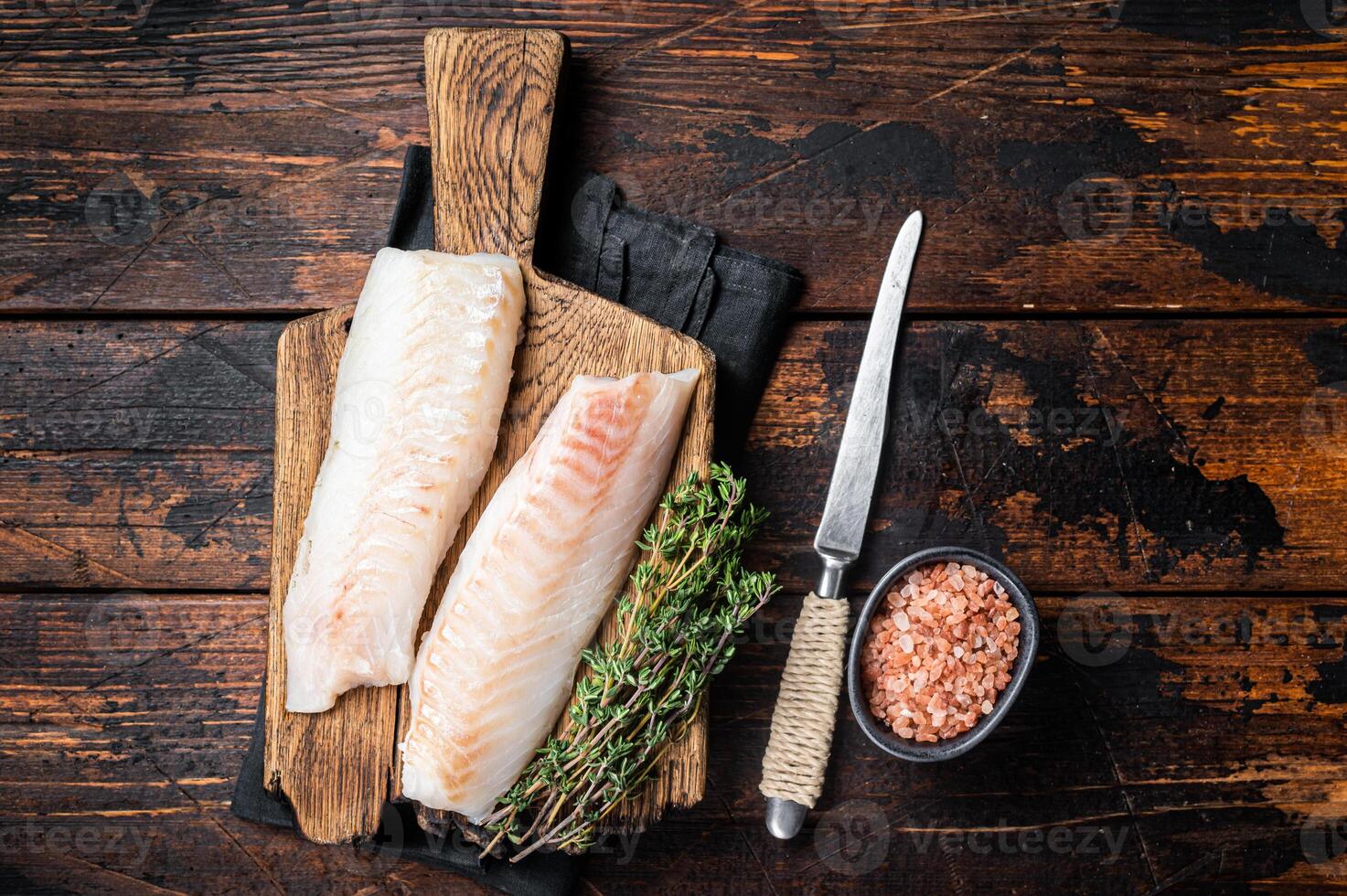 Cod fish fillets, raw codfish with thyme on wooden board. Wooden background. Top view photo