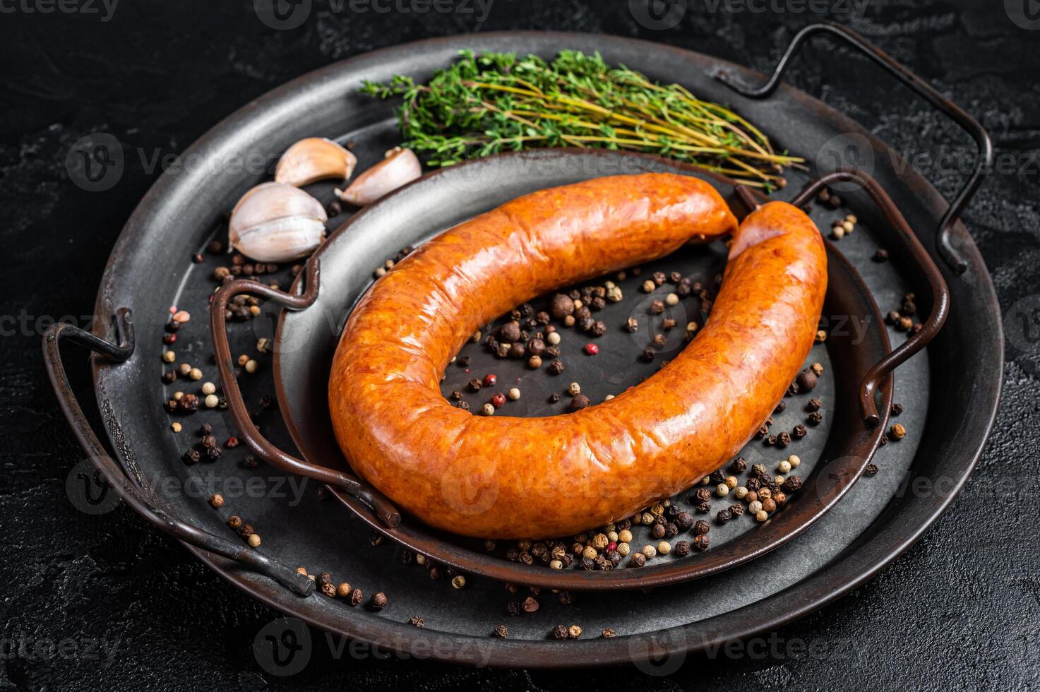 Smoked sausage with thyme and spices in a steel tray. Black background. Top view photo