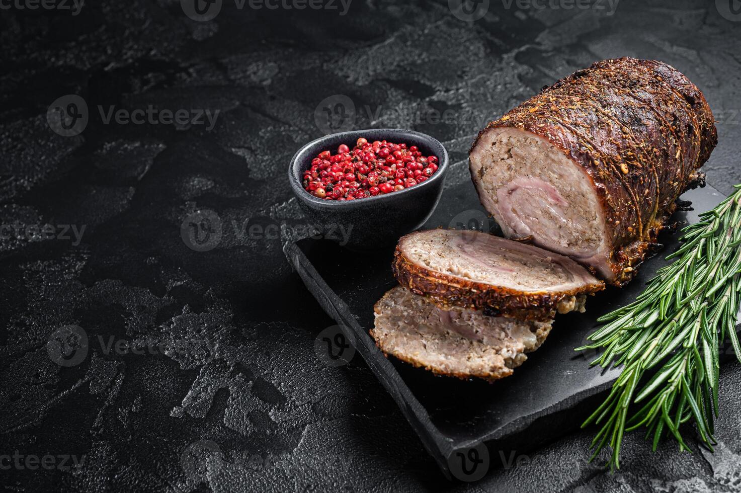 Baked pork roulade Porchetta, rolled pork meat on a marble board with herbs. Black background. Top view. Copy space photo