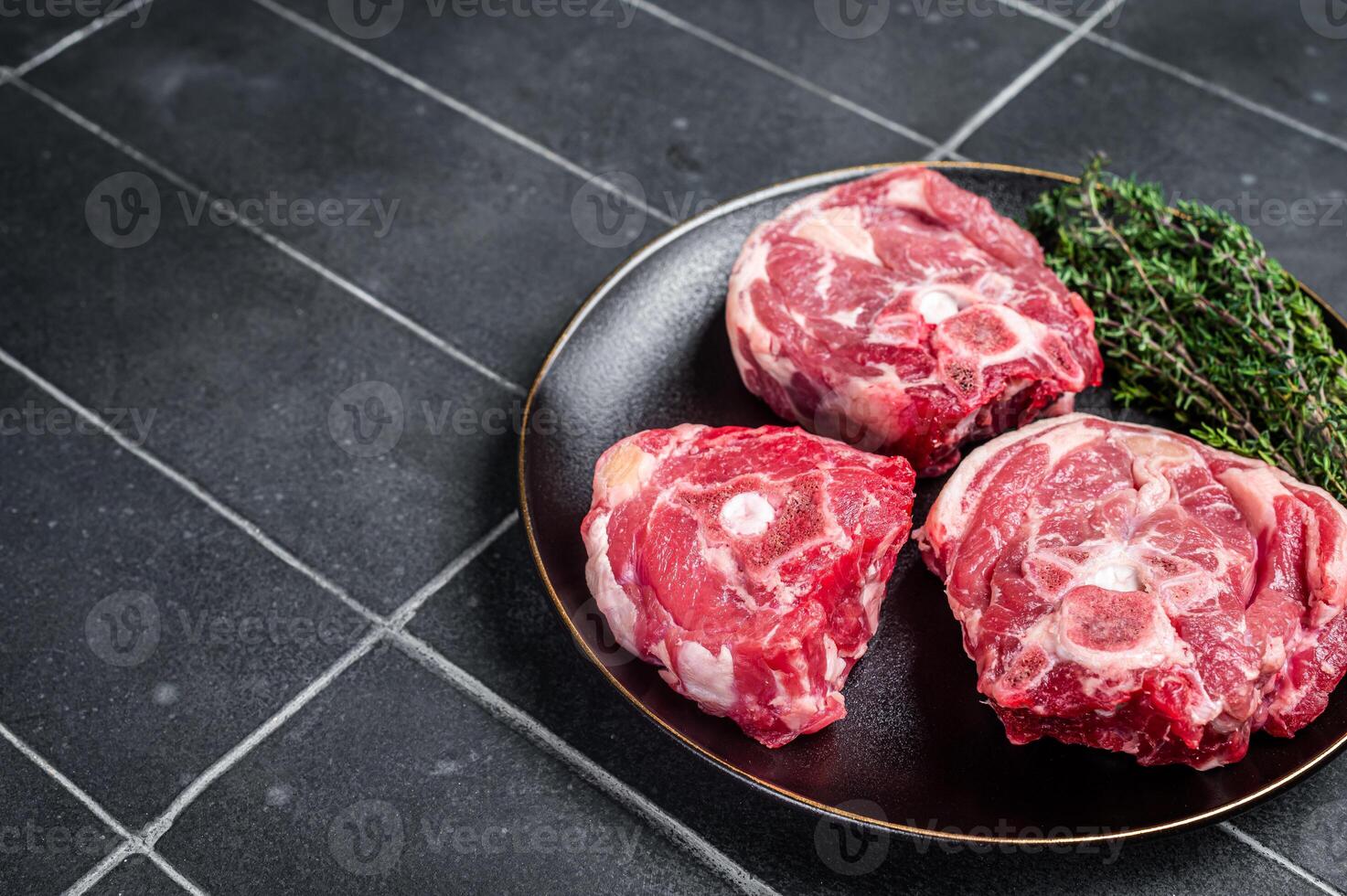 Raw Lamb Gerdan, lamb neck chops on a plate with herbs. Black background. Top view. Copy space photo