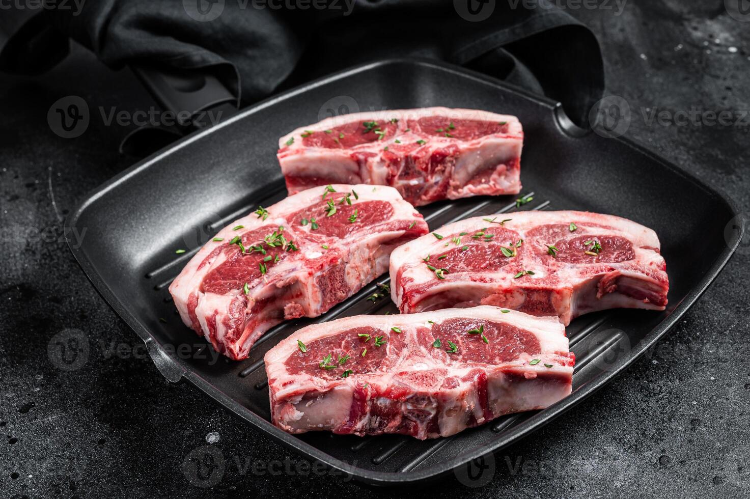 Raw lamb loin rib chops steaks in grill skillet with rosemary and thyme. Black background. Top view photo